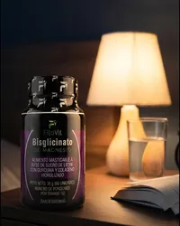 El frasco de bisglicinato de magnesio Fitovit en la mesa de noche, junto a la lámpara y un vaso de agua
