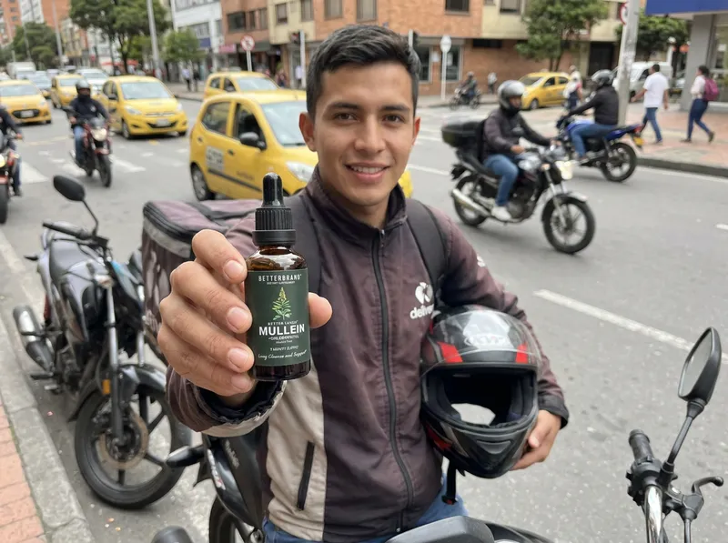 Domiciliario colombiano junto a su moto en la calle con el frasco de gotas